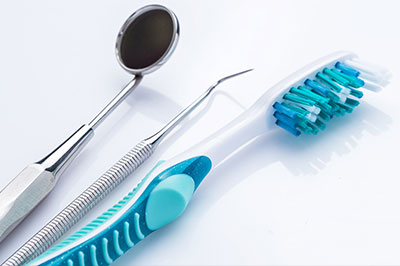 The image features dental tools including a toothbrush with blue bristles and a pair of silver scissors, placed next to each other on a white surface.