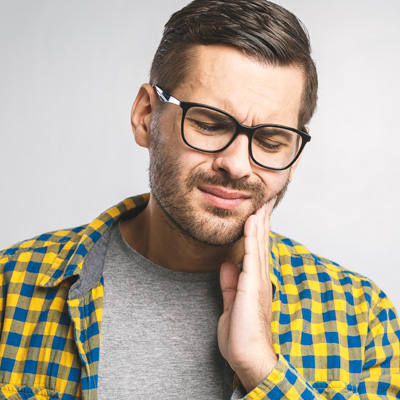 A man with glasses and a beard, wearing a yellow plaid shirt, holding his hand to his mouth in a thoughtful pose.
