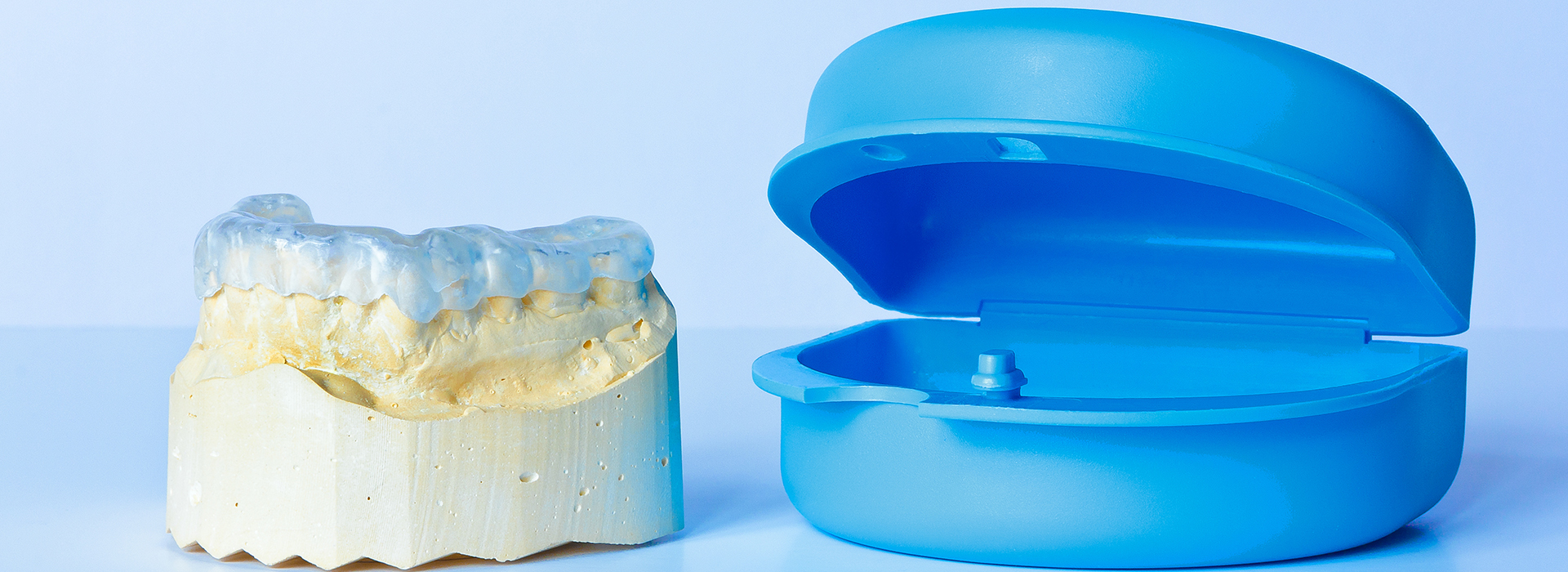 The image displays two dental implants, one on the left appearing yellowed and one on the right with a blueish hue, both set against a white background.